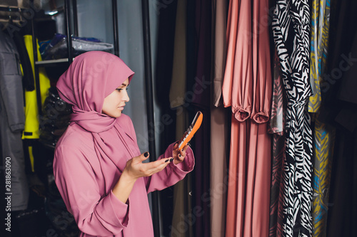 Portrait of a muslim businesswoman checks availability of goods by using the touch pad while standing in her modern shop, young female consultant holding digital tablet during work in fashionable photo