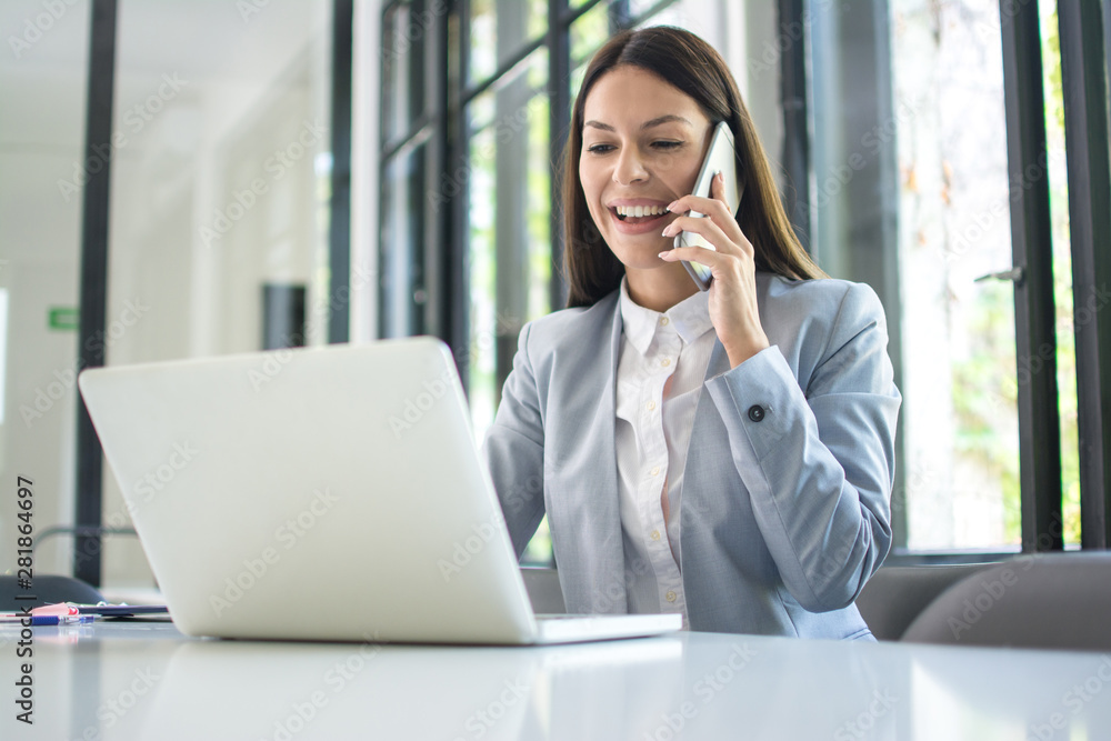 Smiling businesswoman talking on mobile phone and using laptop in office Smiling businesswoman talking on mobile phone and using laptop in office