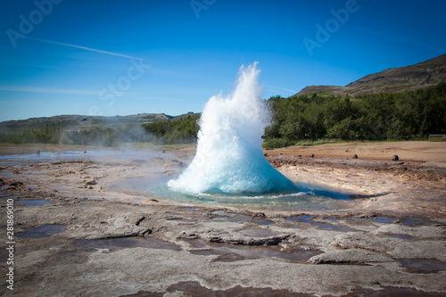 Fototapeta Geyser in Iceland against the blue sky and forest