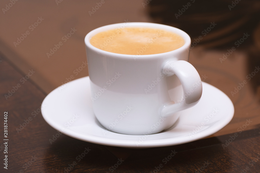 Closeup to white cup of espresso coffee on glass and wooden table 