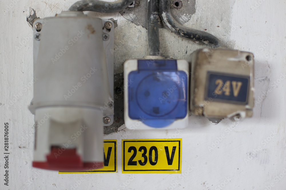 Worn out 400v, 230v and 24 industrial and multiphase power plugs and sockets on a dirty wall inside a workshop
