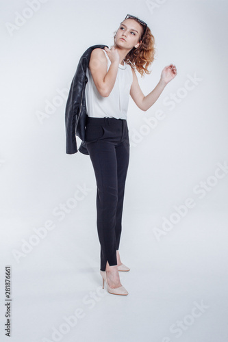 Pretty young fashion sensual woman posing on white background with dressed in hipster style leather jacket outfit. Stylish fashionable girl hipster in black clothes and white shirt.
