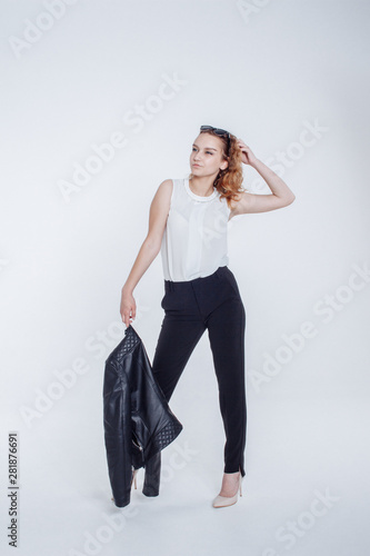 Pretty young fashion sensual woman posing on white background with dressed in hipster style leather jacket outfit. Stylish fashionable girl hipster in black clothes and white shirt.