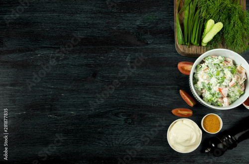 SALAD WITH VEGETABLES ON BACKGROUND. VIEW FROM TOP. FRESH SALAD IN A PLATE ON A DARK BACKGROUND. GARLIC, TOMATO, OGURSKY, UKROP AND ONIONS IN A CERAMIC PLATE ON A DARK TEXTURED SURFACE. COPY SPACE photo