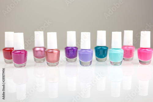 Group of bright multicolor nail polishes in a raw with reflection on a white table