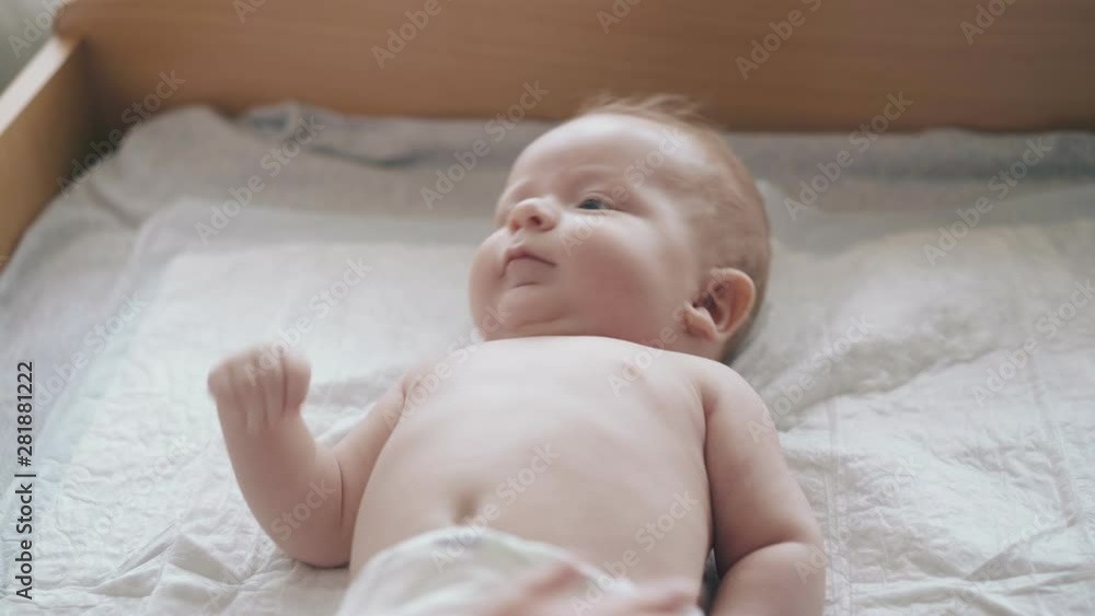 adorable fair haired infant in white diaper with hypertonus lies on changing table and enjoys legs massage close view adorable fair haired infant in white diaper with hypertonus lies on changing table and enjoys legs massage close view