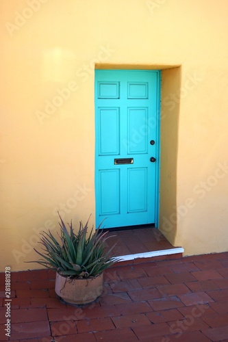 Pale turquoise painted door set in pastel yellow stucco wall with potted plant nearby