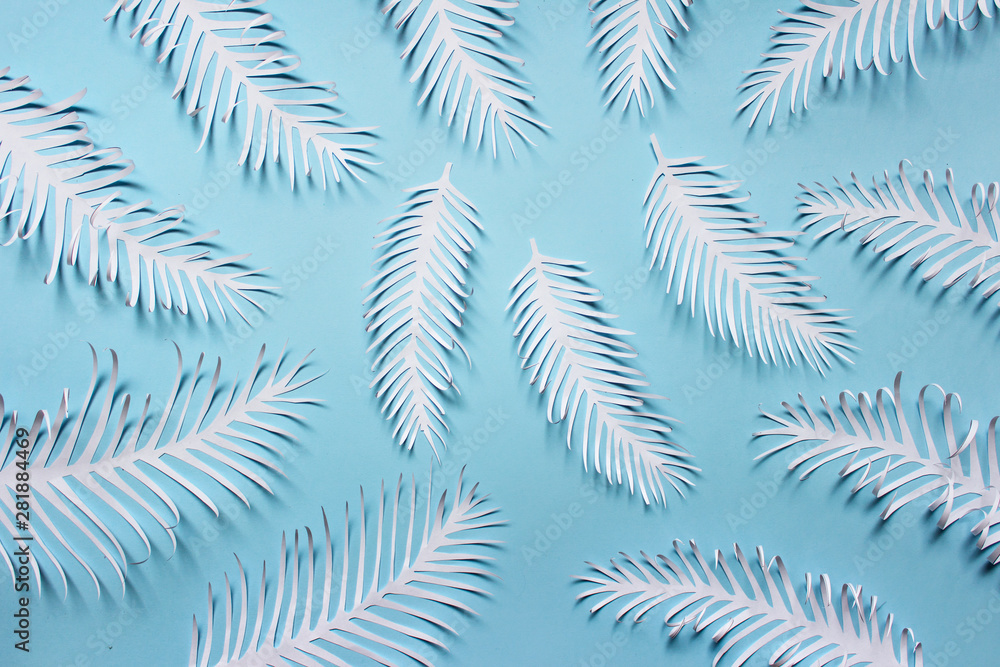 Pattern made of white paper handmade white spiky tropical plant leaves feathears arranged on blue background.