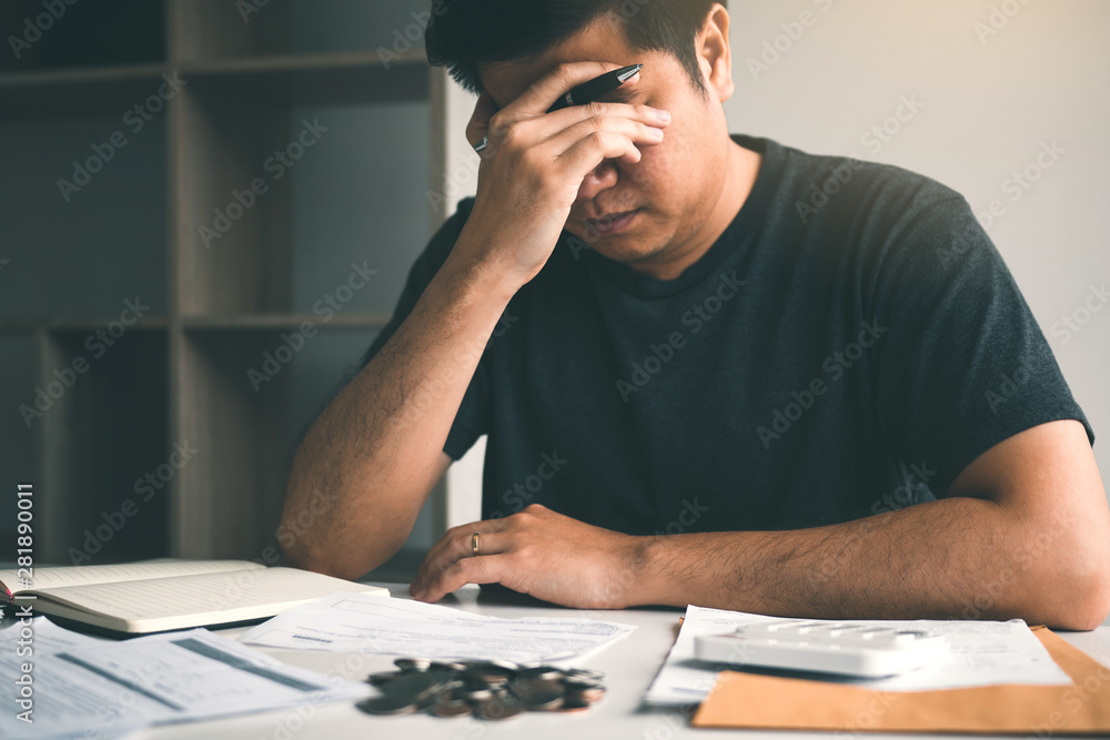 Asian men are stressed about financial problems, with invoices and calculators placed on the table while having stress on problems with home expenses.