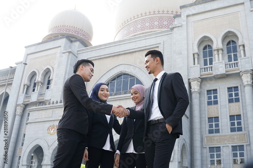 Muslim Asian business people shaking hands with new partner, business co-working teamwork concept. Successfull entrepreneur over a blur majestic building photo