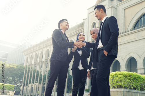 Muslim Asian business people shaking hands with new partner, business co-working teamwork concept. Successfull entrepreneur over a blur majestic building