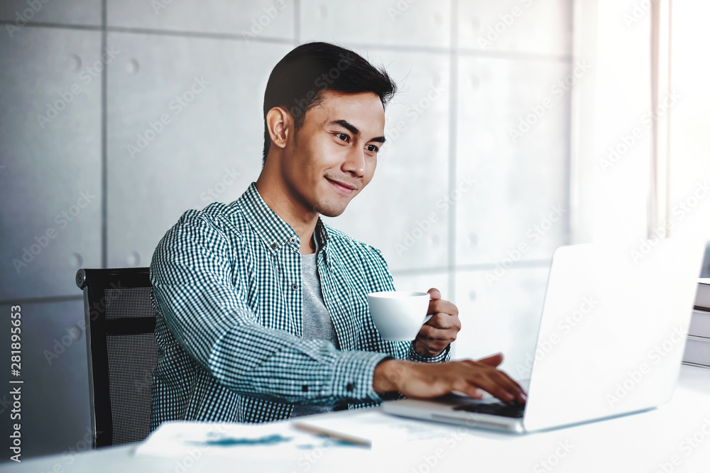 Happy Young Businessman Working on Computer Laptop while Drinking Coffee in Office Happy Young Businessman Working on Computer Laptop while Drinking Coffee in Office