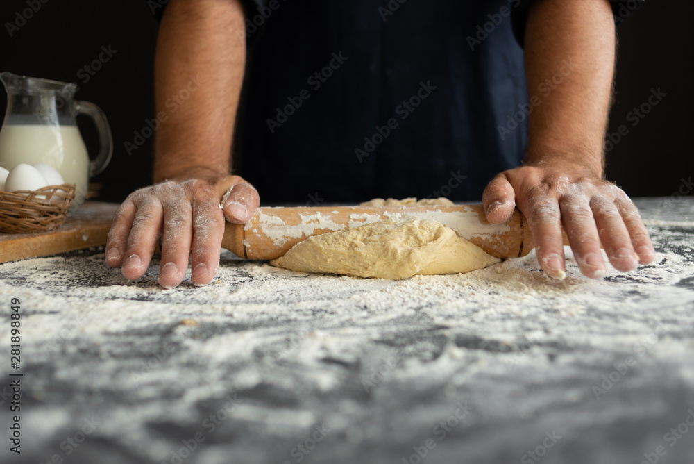a man prepares dinner at home, strong hands roll a roll of raw dough with a rolling pin a man prepares dinner at home, strong hands roll a roll of raw dough with a rolling pin