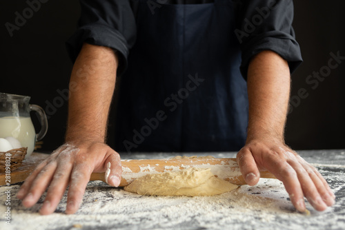 the process of rolling out the dough, male hands of the chef close-up, flour lies on the table
