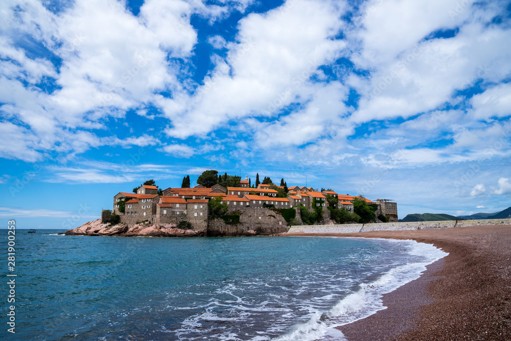Montenegro, Sand beach next to famous little islet sveti stefan with ancient stone houses and red roofs on rocky island in summer holiday