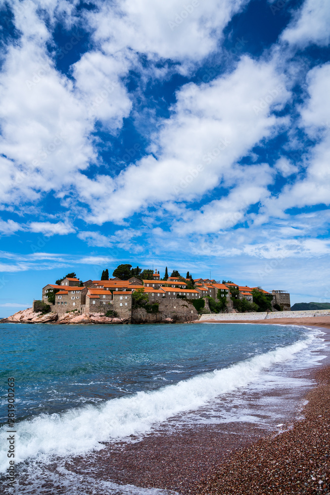 Montenegro, Beachfront at famous little rocky islet sveti stefan with ancient stone houses and red roofs in summer holiday