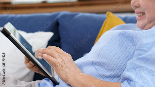 Close up of senior asian woman hand using digital tablet computer while sitting on sofa at home background, Happy retirement asian woman and digital tablet, Active senior people and technology