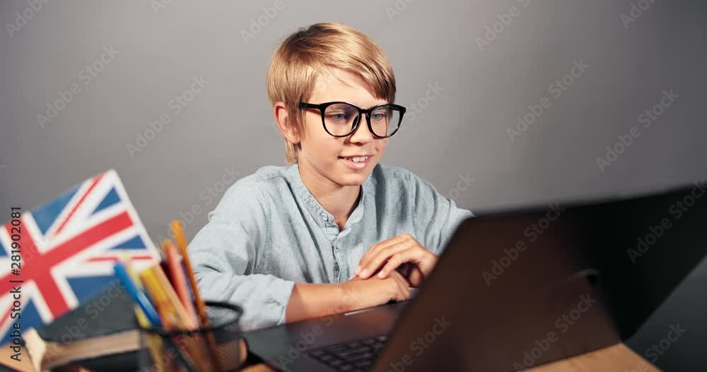 Smiling smart boy making english assignment on laptop, modern technologies in education, online Smiling smart boy making english assignment on laptop, modern technologies in education, online