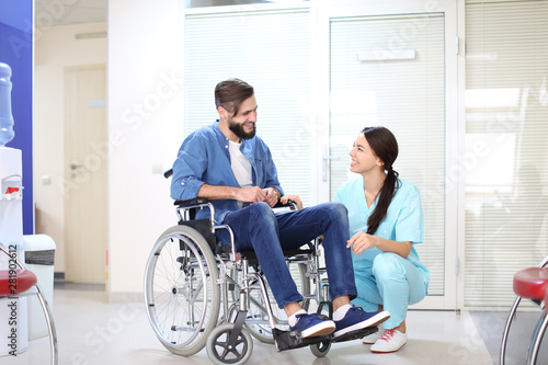 Young female doctor taking care of man in wheelchair indoors