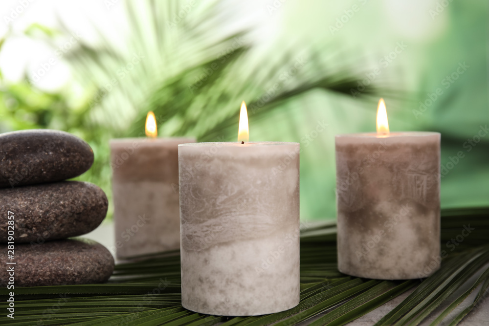 Burning candles and spa stones with palm leaf on table against blurred green background Burning candles and spa stones with palm leaf on table against blurred green background