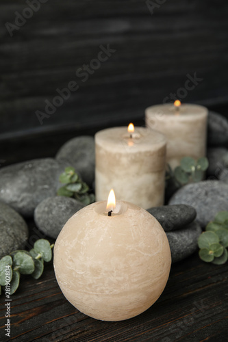 Composition with burning candles, spa stones and eucalyptus on dark wooden table, space for text