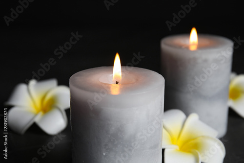 Burning candles and plumeria flowers on black background, closeup