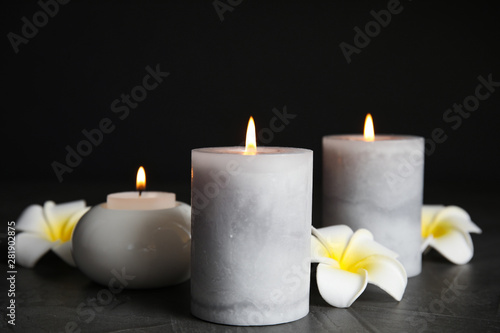 Burning candles and plumeria flowers on dark grey table against black background