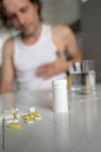Pills and tablets lying on the table. A man holds his hand on his heart. Sickness, malaise, heartache. Foreground. Vertical. Close-up