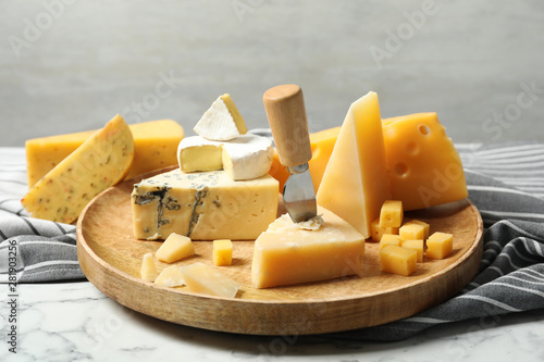 Wooden plate with different types of delicious cheese on marble table against light background photo