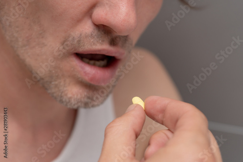 A man holds a yellow tablet, going to drink the medicine. Sickness, malaise, headache, cold. Side view. Close-up