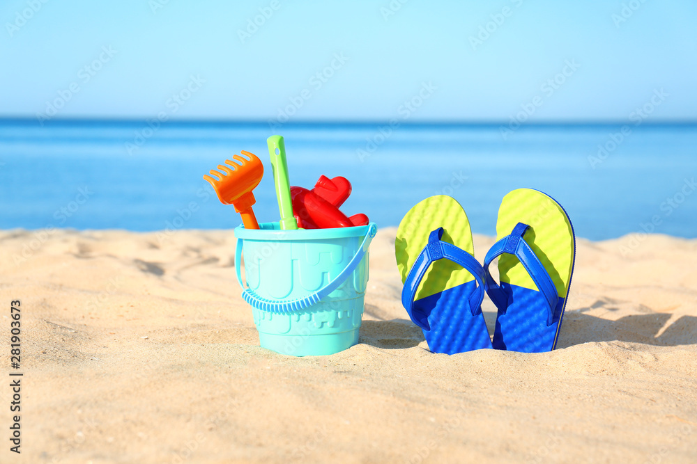 Beautiful view of sand with plastic beach toys and flip flops near sea on sunny day Beautiful view of sand with plastic beach toys and flip flops near sea on sunny day