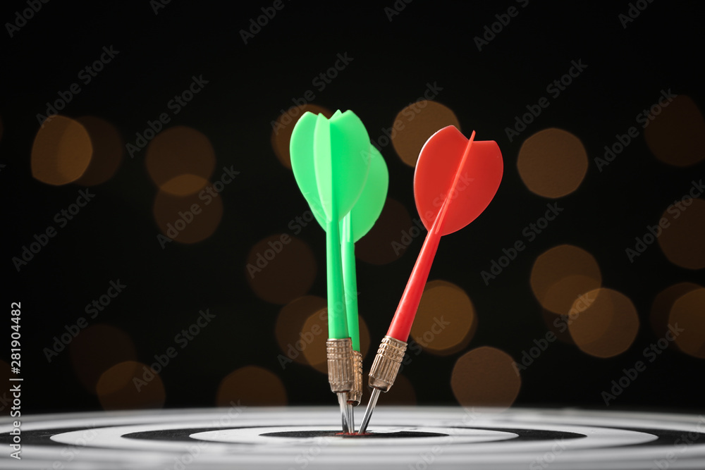 Arrows hitting target on dart board against blurred lights Arrows hitting target on dart board against blurred lights
