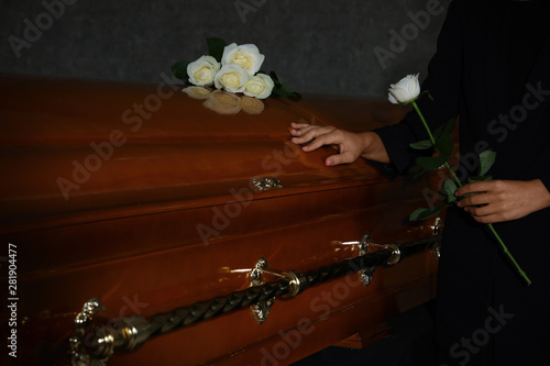 Young woman with white rose near casket in funeral home, closeup