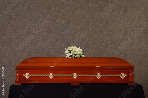 Wooden funeral casket with white lilies at grey wall photo
