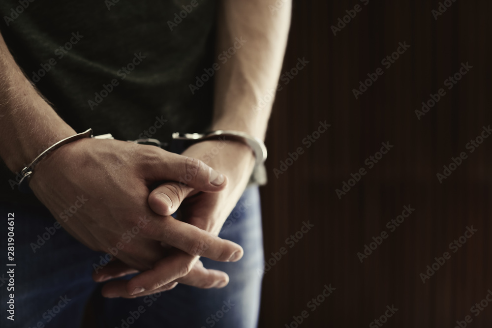 Man detained in handcuffs against blurred wooden background, space for text. Criminal law