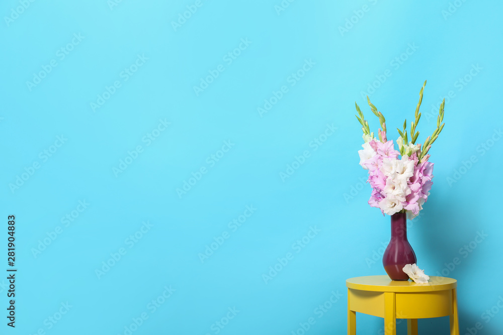 Vase with beautiful gladiolus flowers on wooden table against blue background. Space for text