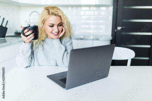 Young blonde woman using laptop in the kitchen at home