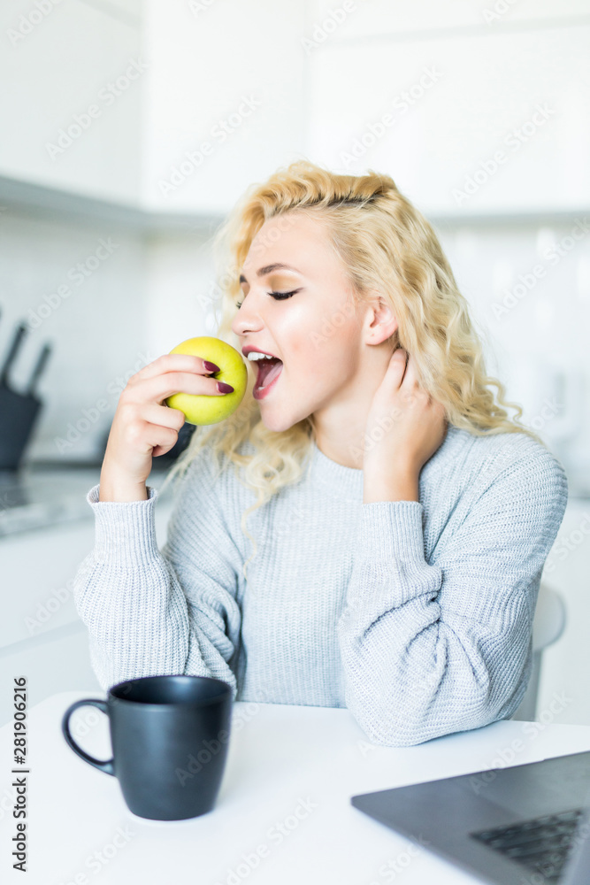 Young woman with green apple and laptop sitting in the kitchen Young woman with green apple and laptop sitting in the kitchen
