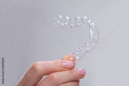 Woman's Hand Holding Plastic Braces Over Gray Backdrop