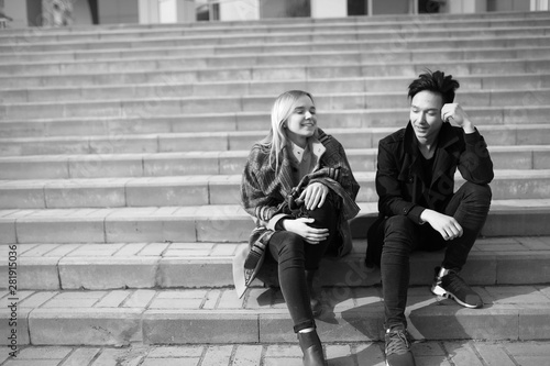 A pair of young people met in the park. Lovers are sitting on a bench in the city autumn park. An Asian boy and a white girl sitting on a park bench.