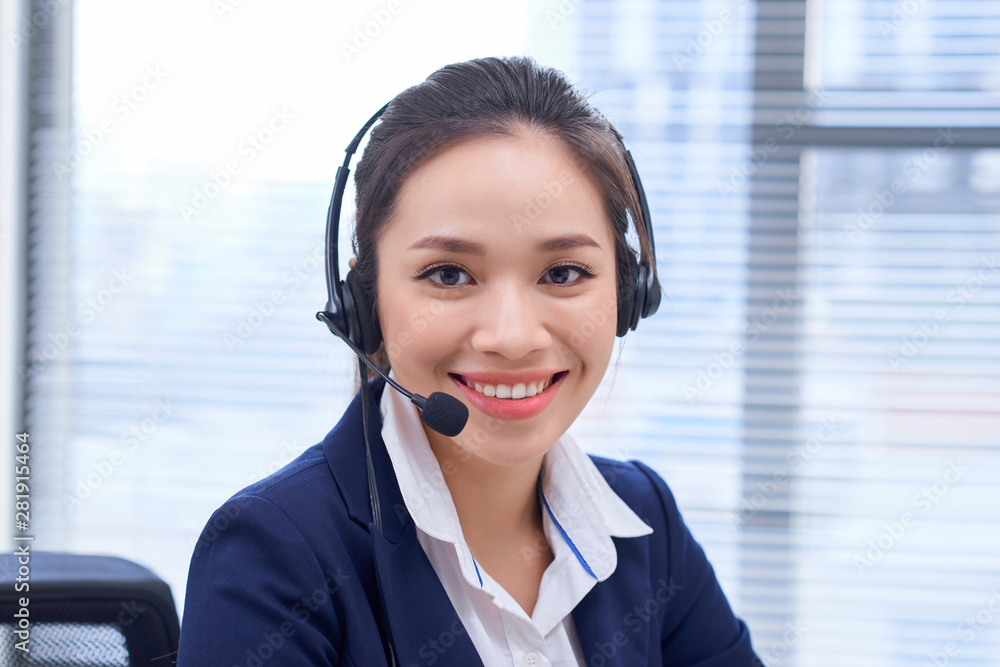 Portrait of happy smiling female customer support phone operator at workplace. Asian Portrait of happy smiling female customer support phone operator at workplace. Asian