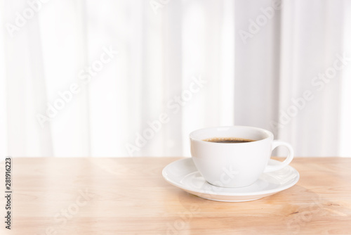 White coffee cup on wooden office desk with morning sunlight and soft curtain background