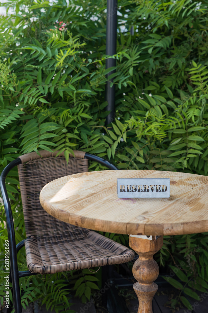 Table reservation sign close up. Reserved sign on summer restaurant outdoor terrace wooden table with green leaves. Interior of trendy cafe bistro, place settings and decor with copy space. Table reservation sign close up. Reserved sign on summer restaurant outdoor terrace wooden table with green leaves. Interior of trendy cafe bistro, place settings and decor with copy space.