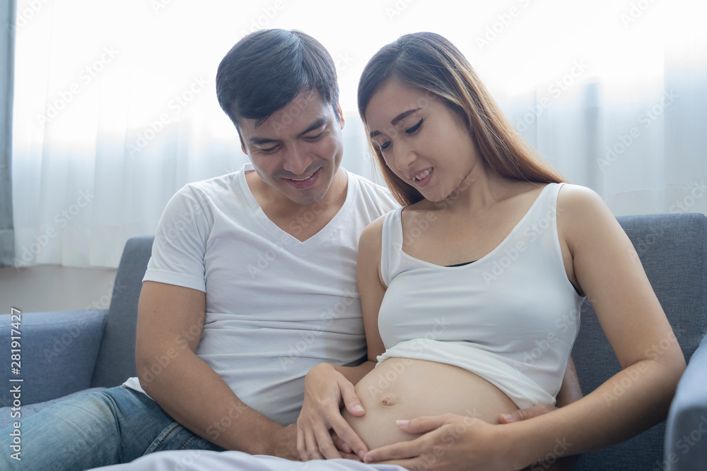Beautiful pregnant woman and her handsome husband are smiling while spending time together in sofa. Beautiful pregnant woman and her handsome husband are smiling while spending time together in sofa.
