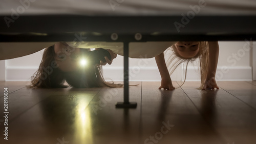 Mother and daughter shine a flashlight looking under the bed