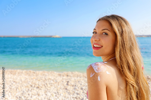 Young woman with sun shape on the shoulder. Beautiful happy cute woman applying suntan cream on her shoulder with beach background. Copy space.