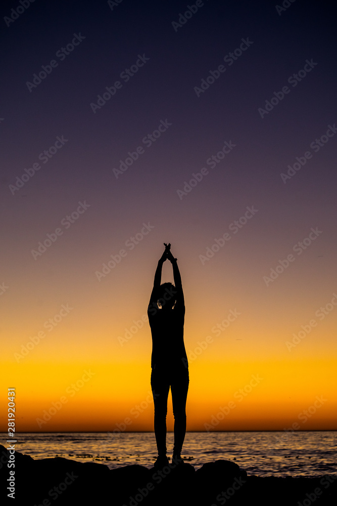 silhouette of woman doing yoga on the beach at sunset