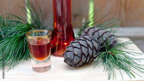 a glass liquor, cones and twigs from the swiss stone pine or arolla on a wood board photo