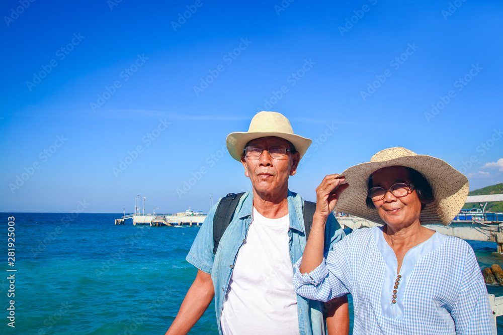 An elderly Asian couple standing hugging each other, happy at the sea.