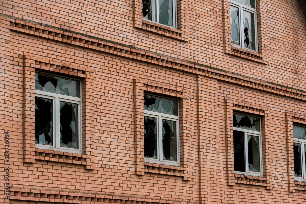 The wall of an abandoned brick house with broken glass in the Windows. The concept of chaos The wall of an abandoned brick house with broken glass in the Windows. The concept of chaos